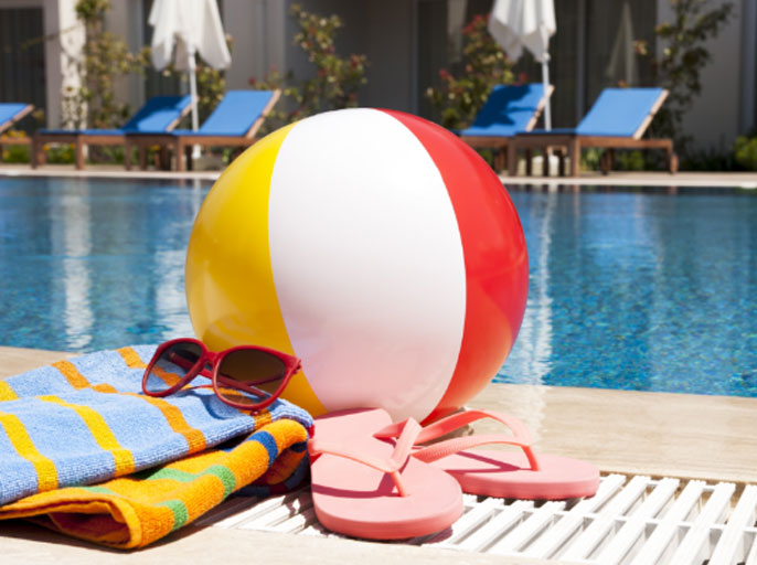 Beach ball with towel and flip flops by a pool