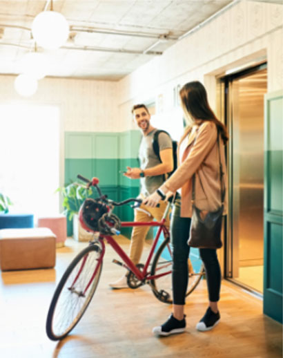 A woman with a bicycle walks off an elevator with a man