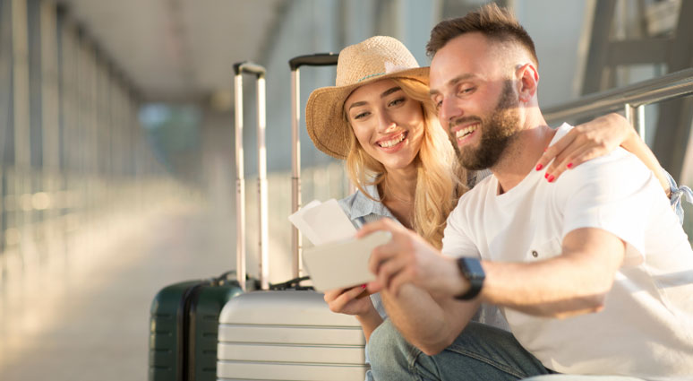 A couple looks at their tickets in an airport, with luggage