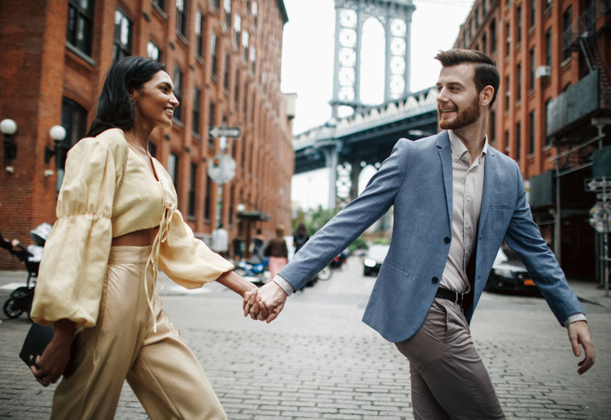 A couple holding hands while crossing the street in front of a bridge